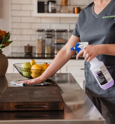 Merry Maids of Lancaster County cleaner disinfecting a kitchen counter with eco-friendly spray during a recurring house cleaning.
