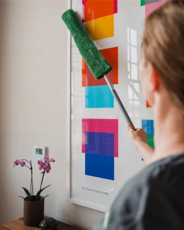 Merry Maids of Berks County cleaner carefully dusting a framed art print with a microfiber duster